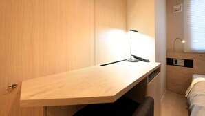 Une pièce de taille modeste, comprenant un bureau en bois, une chaise, un lit et une table de chevet.