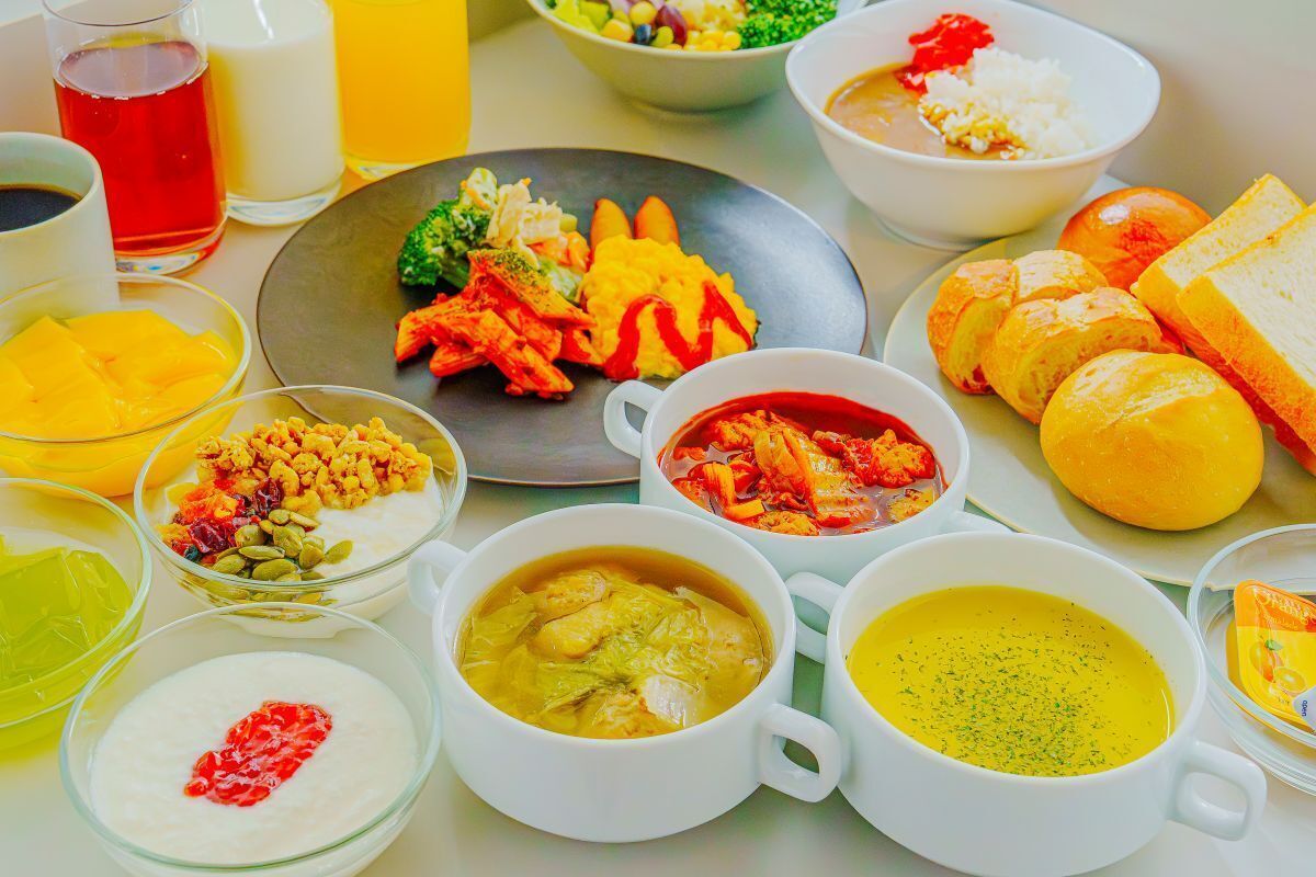 A table with various dishes, including a plate with vegetables, bowls of soup, and a glass of red beverage.