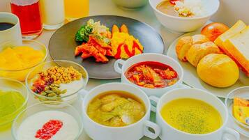 A table with various dishes, including a plate with vegetables, bowls of soup, and a glass of red beverage.