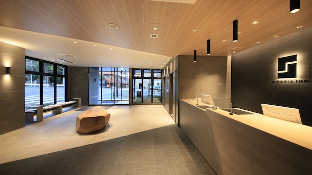 Un espace d’accueil moderne, avec un plafond en bois, un comptoir de réception et un coin salon agrémenté d’un banc au design géométrique original.