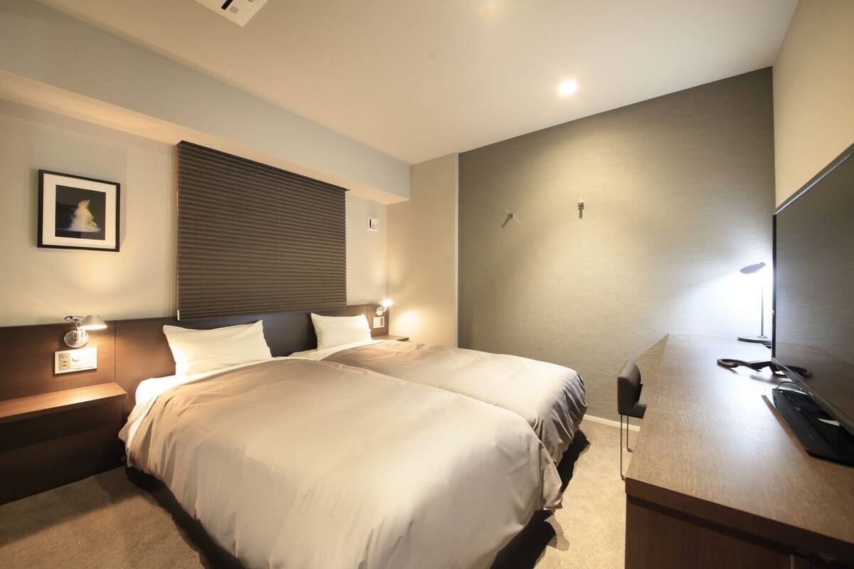 A double bed with a headboard, bedside tables with lamps, a flat-screen TV, and a wall-mounted light fixture.