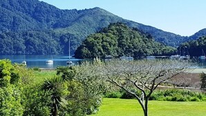 A coastal landscape with a mountain, a small island, and a marina with boats. - Relax and Enjoy - Waterfront Bach in Ngakuta Bay (Ngakuta Bay)