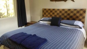 A neatly made bed with striped bedding and two pillows, a headboard with a checkered pattern, and a wall-mounted fish decoration. - Relax and Enjoy - Waterfront Bach in Ngakuta Bay (Ngakuta Bay)
