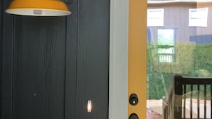 Una puerta de madera oscura con una lámpara amarilla fijada a la pared y un timbre.