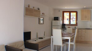 Espai vital compacte amb sofà, taula de dinar, cadires i una petita cuina amb nevera, microones i cafetera.