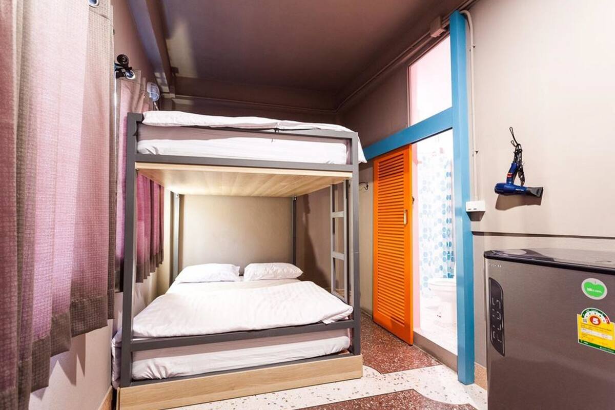 A bunk bed room with a small refrigerator and a window with blinds.