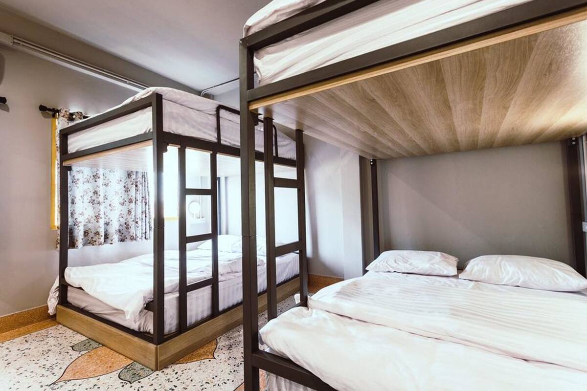 A room with two bunk beds, one with a canopy and one without, a patterned rug, and a window with curtains.