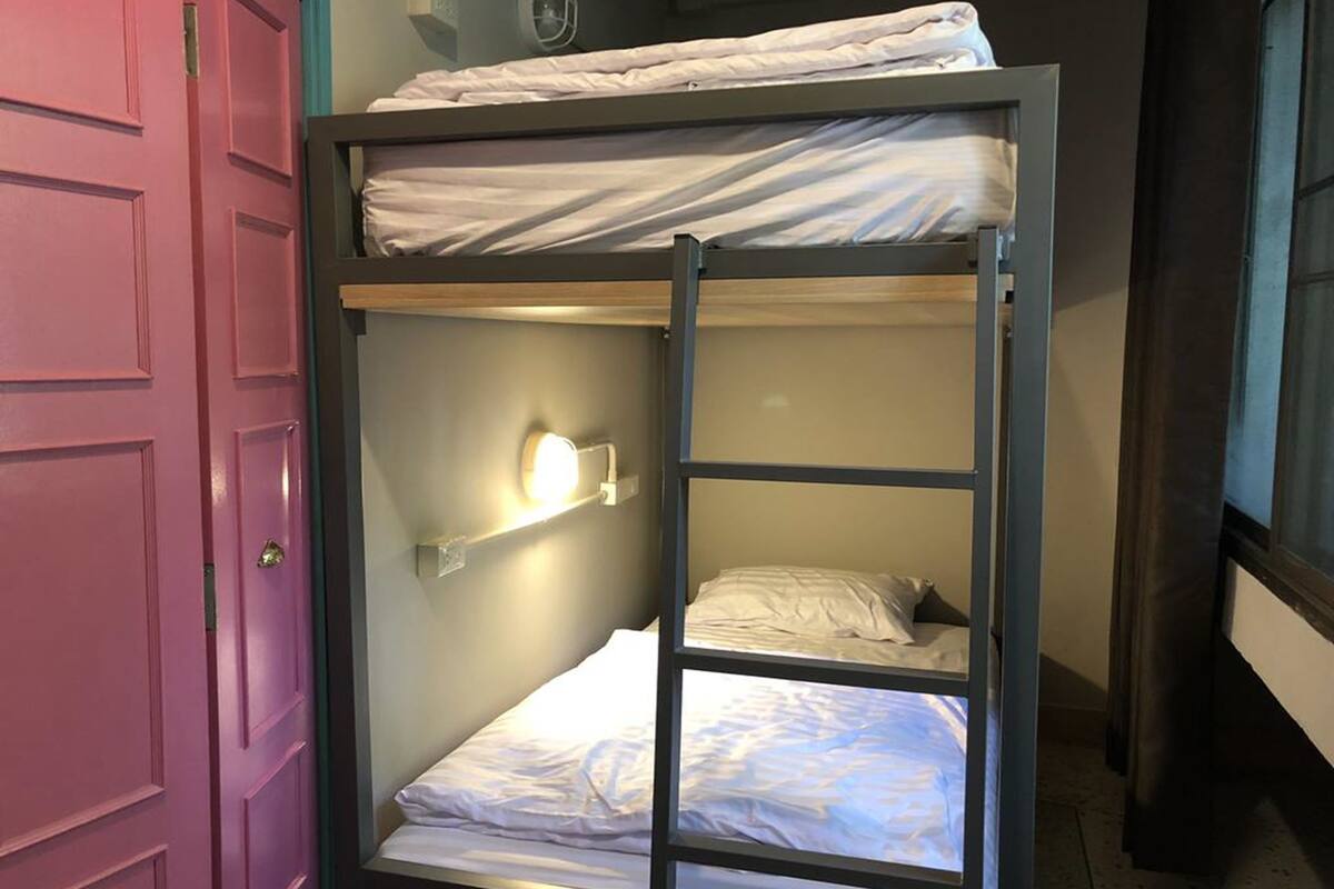 A bunk bed with a ladder, a light fixture on the wall, and a pink door.