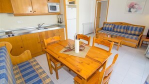 A compact kitchen with wooden cabinets, a microwave, and a sink. There is a dining table with chairs and a sofa with plaid cushions. - Rescator Resort 318 - One Bedroom Apartment, Sleeps 4 (Roses)