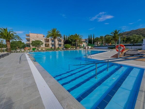 Una piscina con agua azul cristalina, rodeada de palmeras y un edificio moderno al fondo.