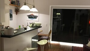 A modern kitchen with a bar area, wooden flooring, and a large sliding glass door leading to a dark room.