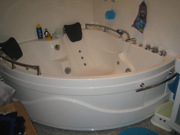 Eine große, weiße, freistehende Badewanne mit mehreren Wasserhähnen und einer integrierten Sitzbank.