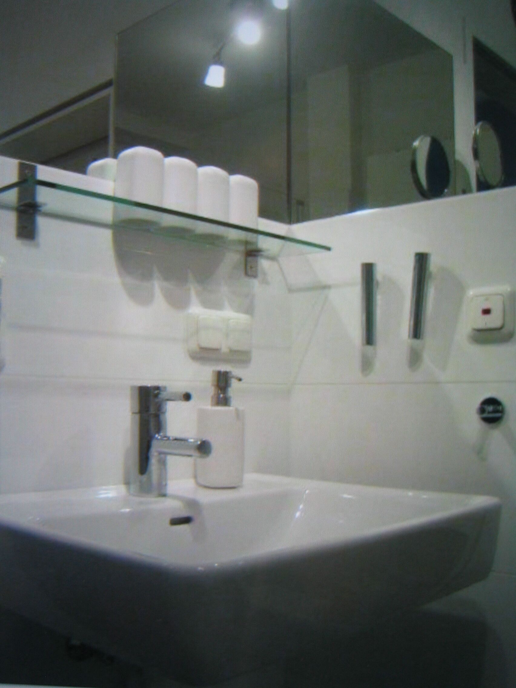 Une salle de bain avec une étagère en verre où sont rangés les articles de toilette, un lavabo avec un robinet et un miroir au-dessus du lavabo.
