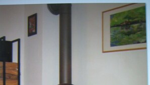 A room with a wood-burning stove, a wicker chair, and a framed painting on the wall.