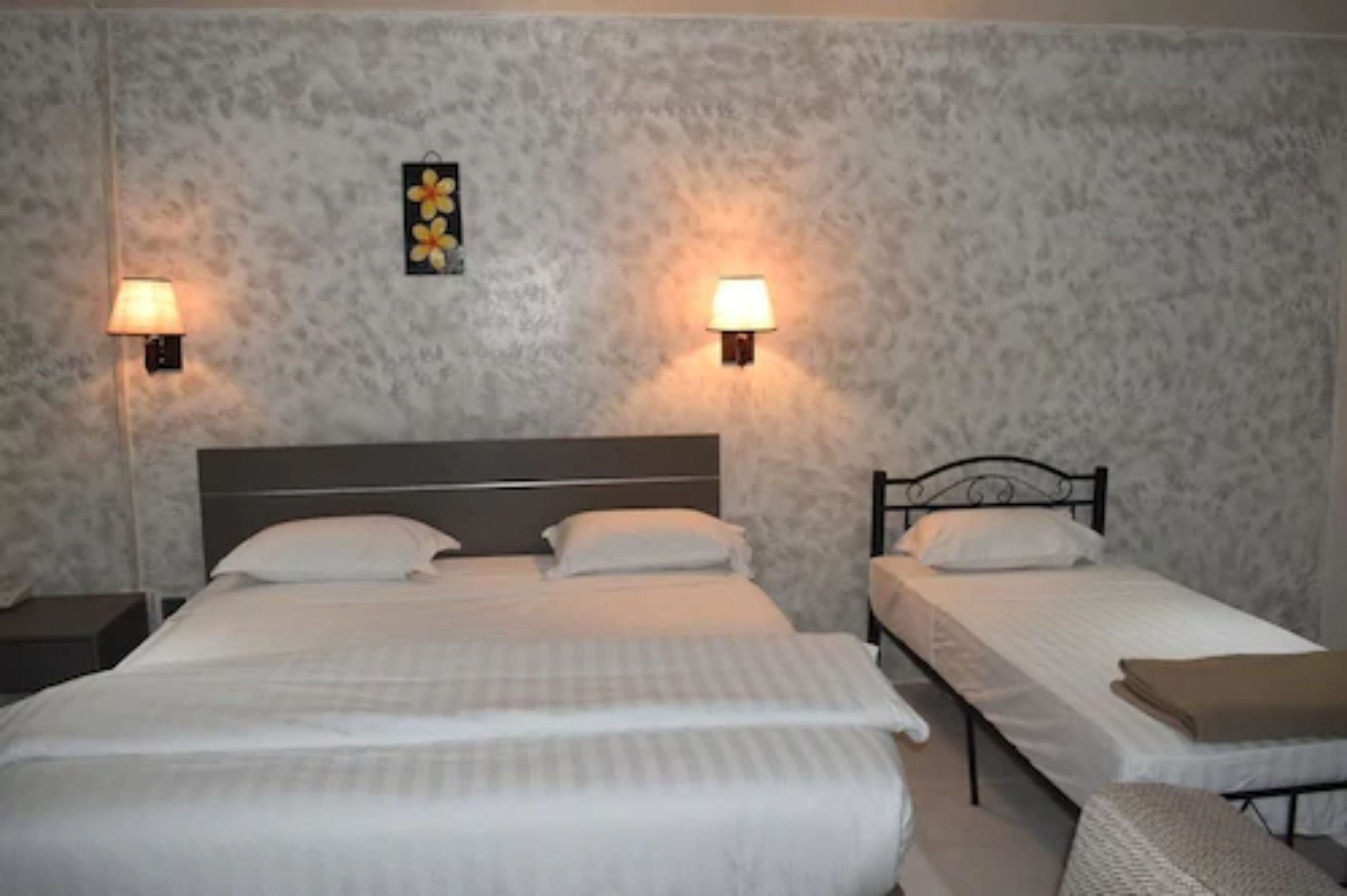 A hotel room with two single beds, a nightstand, and a wall-mounted lamp.