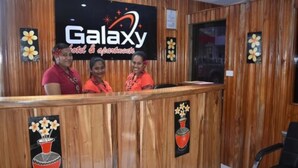 A Galaxy hotel reception desk with wooden paneling and floral artwork. - Galaxy Hotels & Apartments (Labasa)