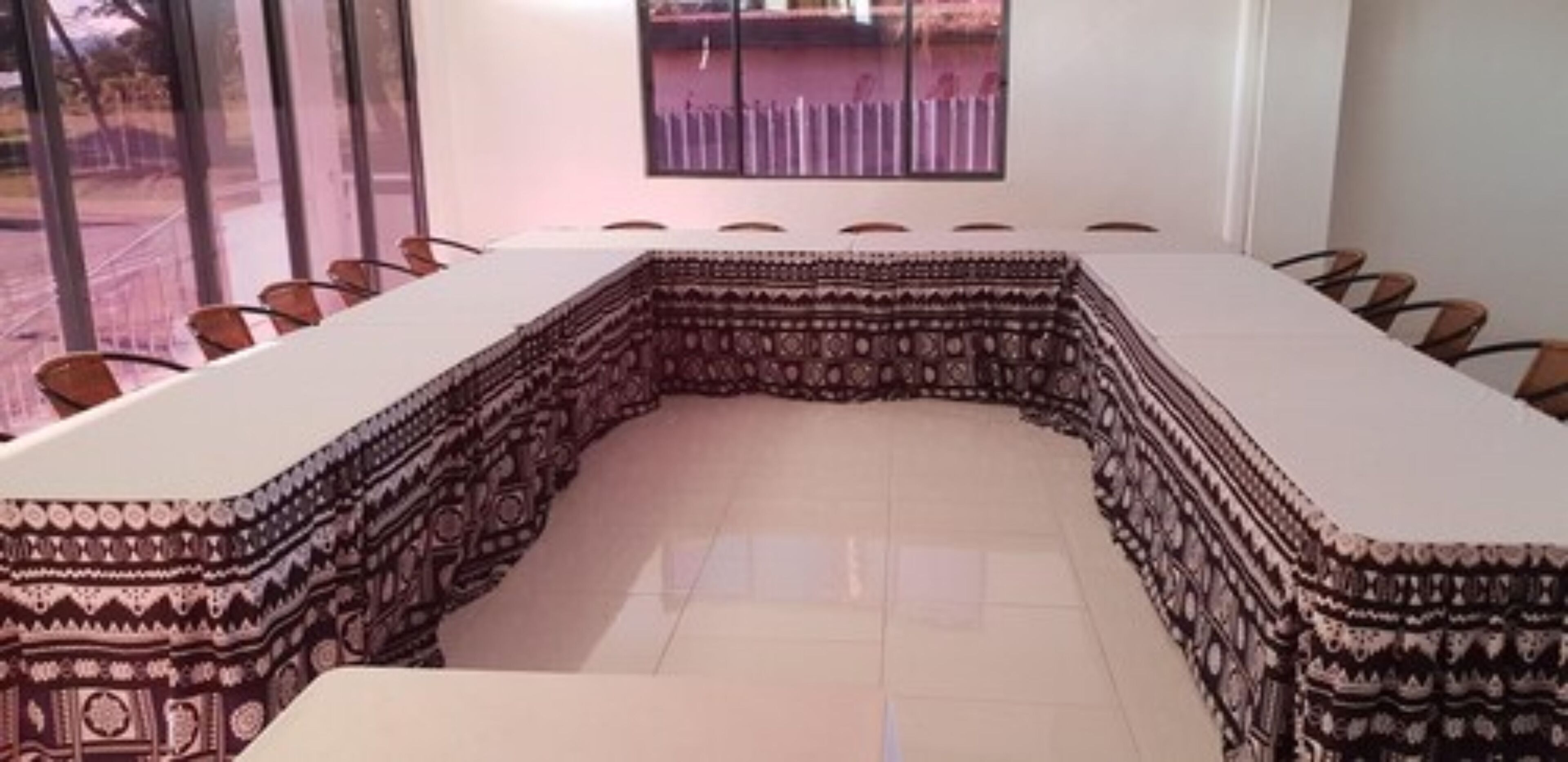 Un salón de conferencias con una mesa grande y curvada rodeada de sillas, un ventanal con vistas a una valla y un suelo de baldosas.