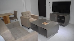 A modern living room with a sofa, armchair, coffee table, TV stand, and a small table. - Galaxy Hotels & Apartments (Labasa)
