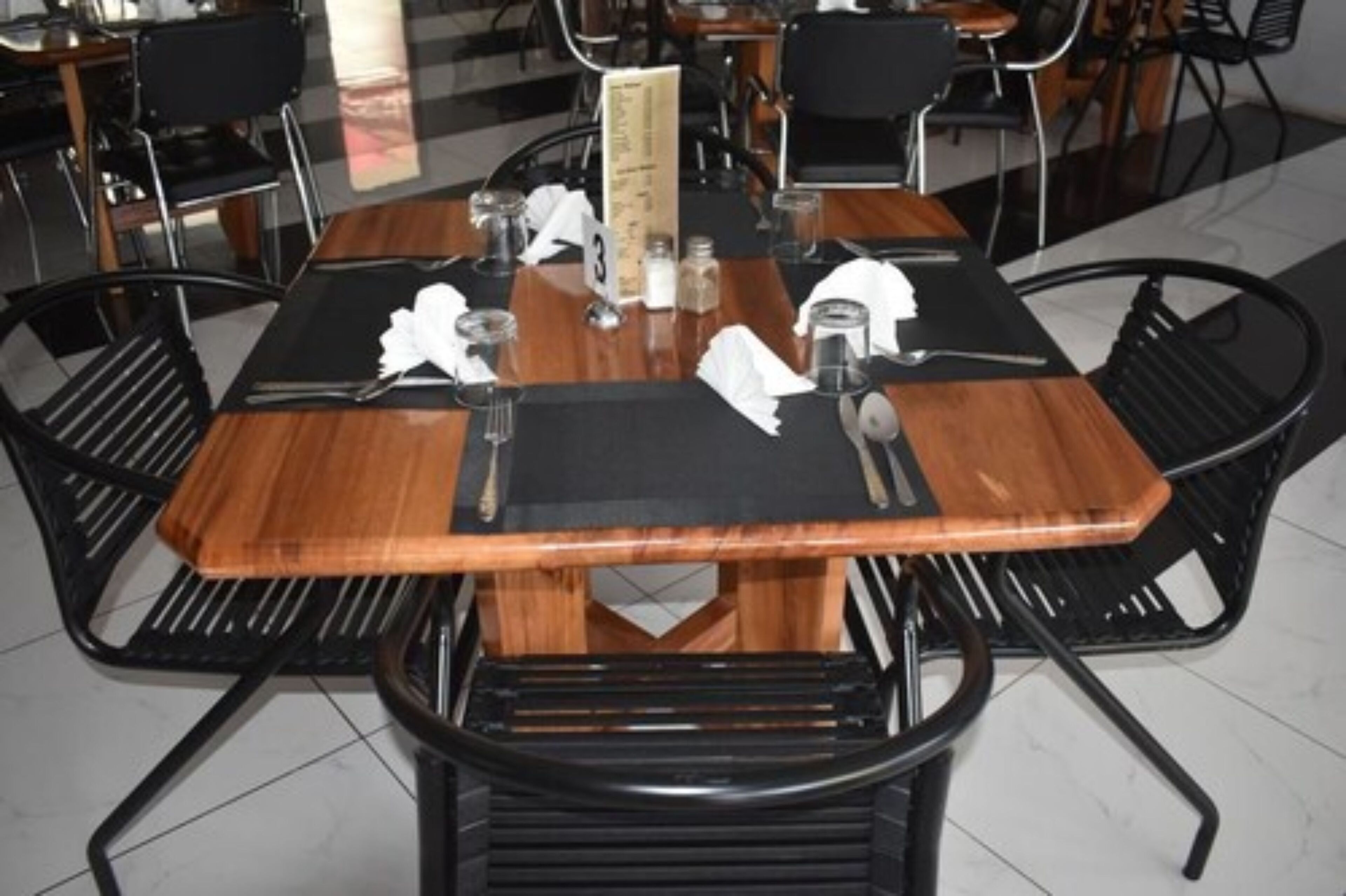 A dining table with a black placemat, set with white napkins, cutlery, and glasses.