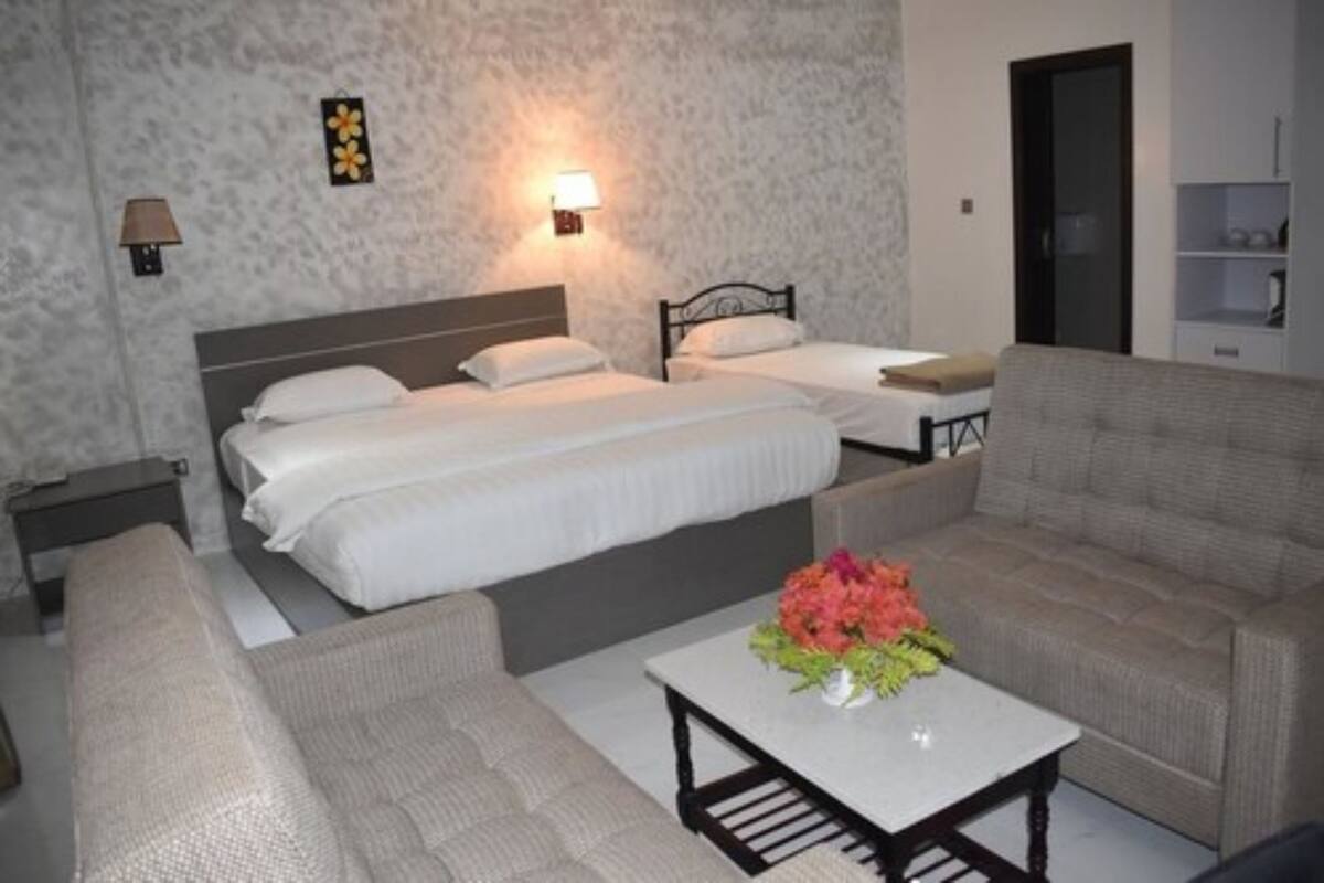 Habitación de hotel con dos camas, un sofá, una mesita y una lámpara de pared.