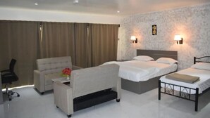 A hotel room with two beds, a sofa, a desk, and a chair. There are wall-mounted lamps and a window with curtains. - Galaxy Hotels & Apartments (Labasa)
