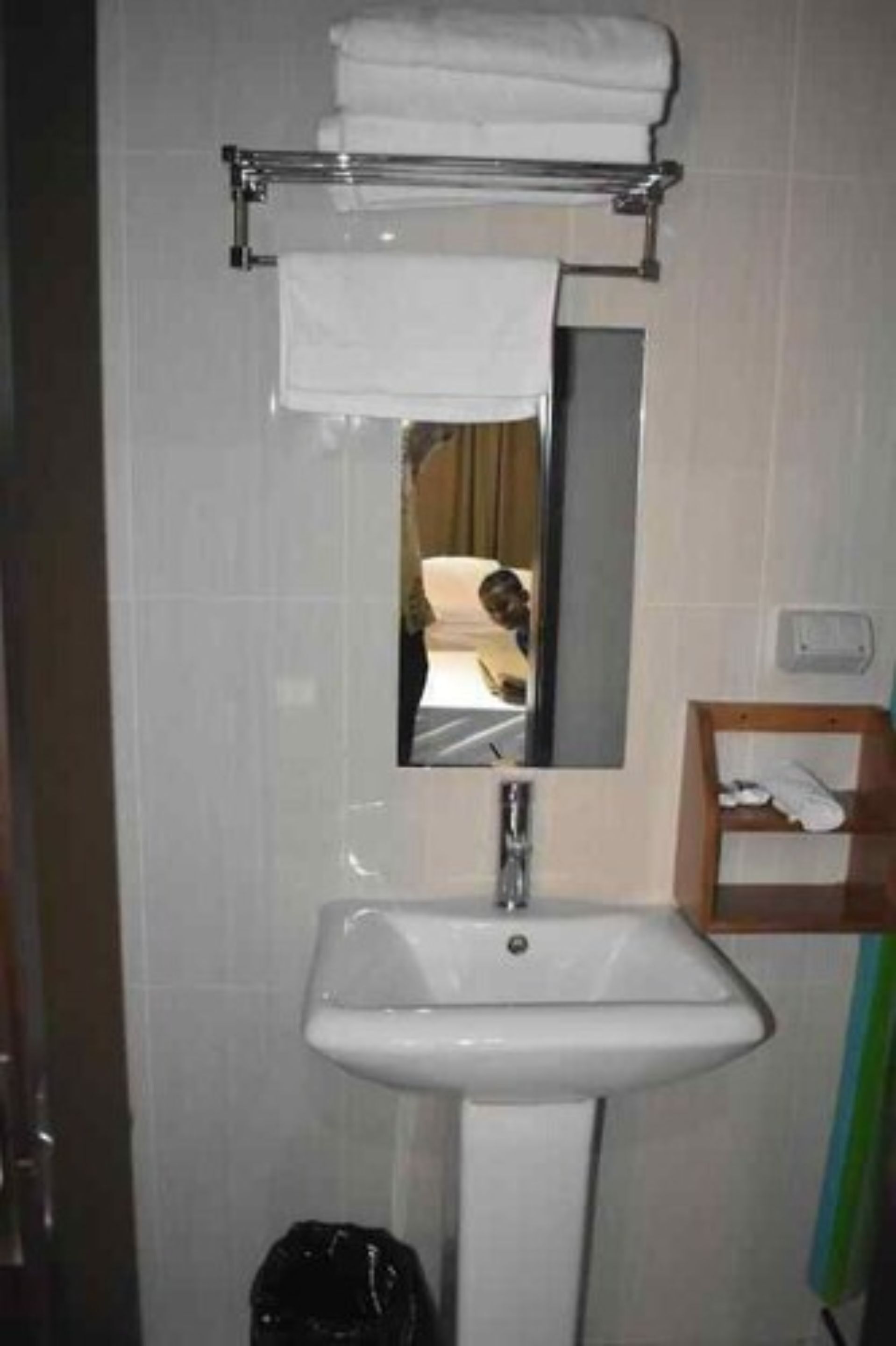 Un baño con un lavamanos blanco, un espejo y un perchero para toallas.