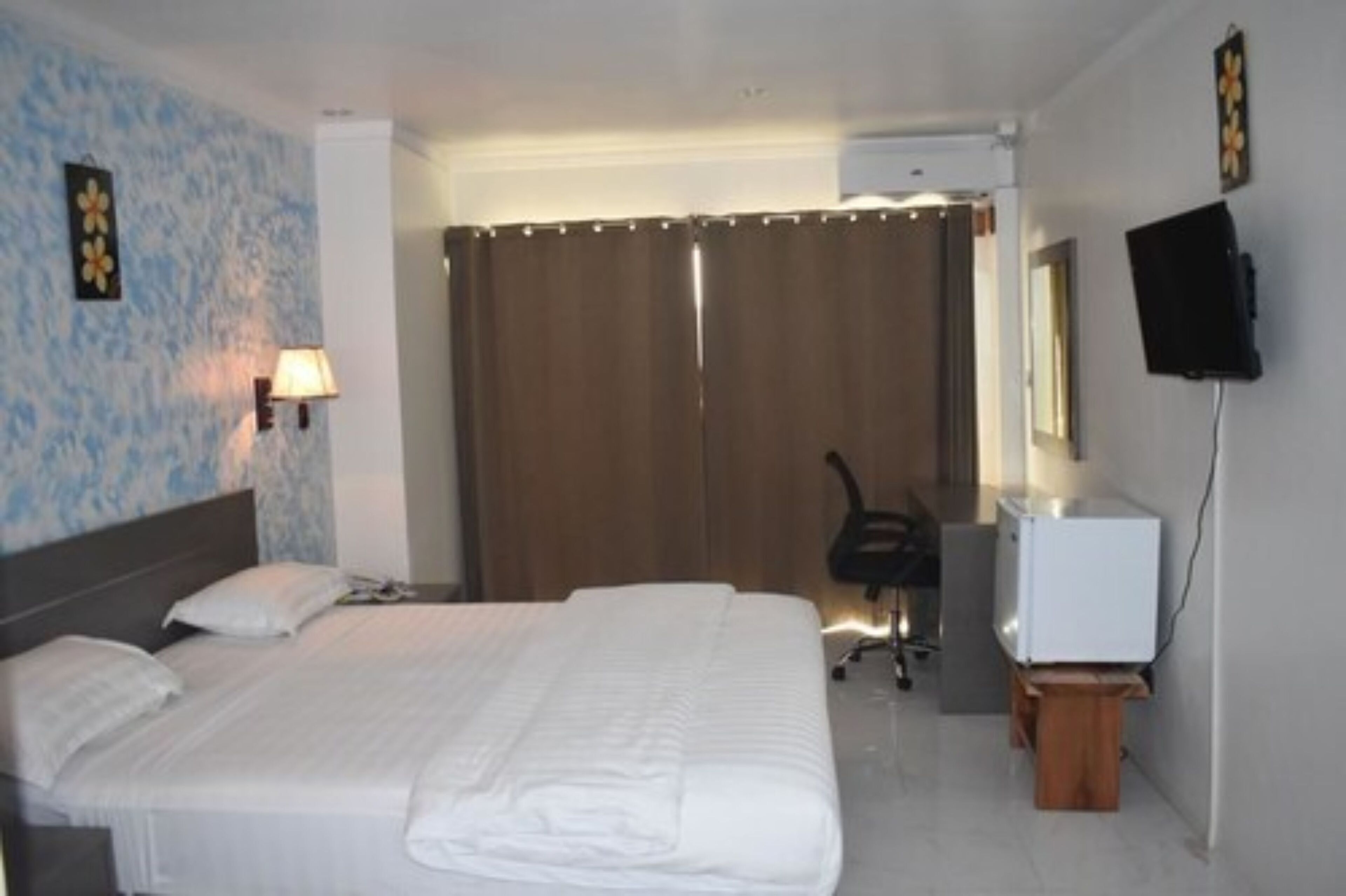 Habitación de hotel con una cama grande, un escritorio con ordenador, un televisor y zona de ducha.
