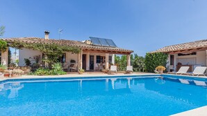 Una piscina con solárium de baldosas, un porche cubierto y plantas en macetas.