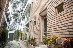 A brick building with a narrow pathway, potted plants, and a small window.