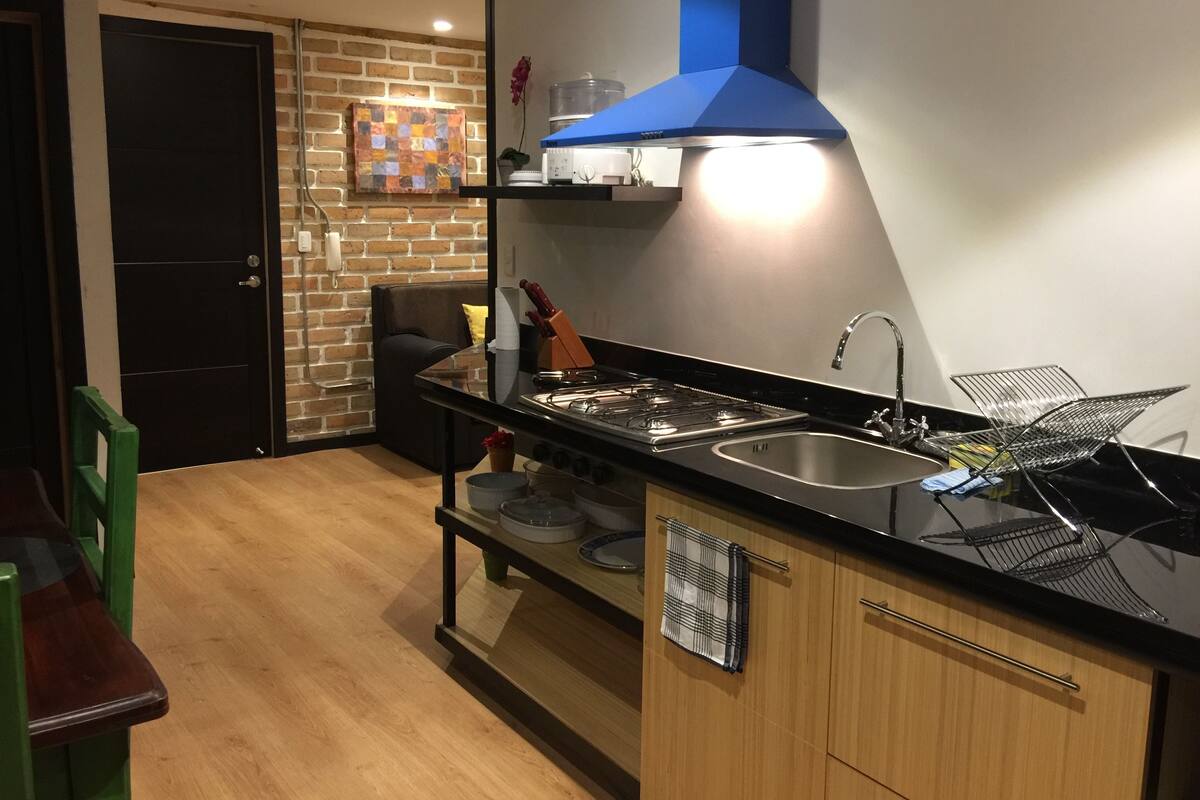 Ett modernt kök med en gasspis, en diskho i rostfritt stål och en blå köksfläkt.