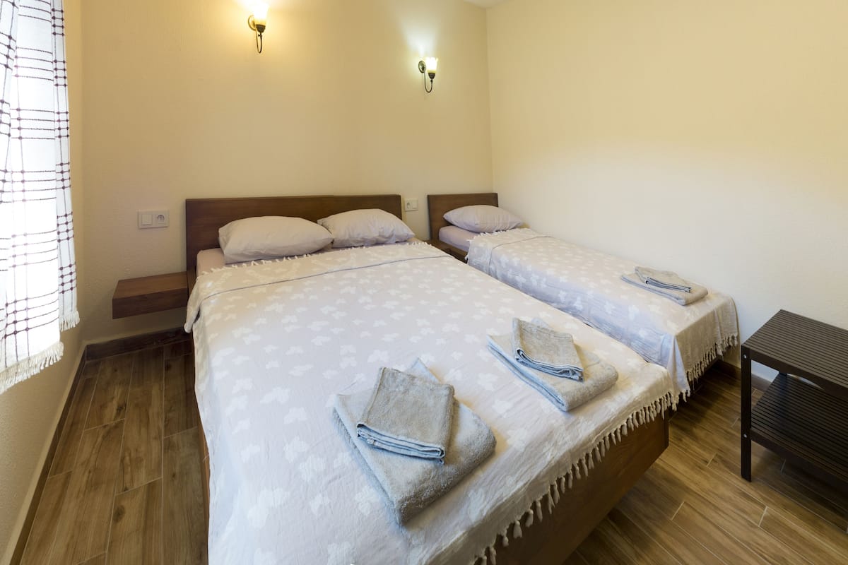 A room with two beds, each with a headboard, a small table, and a wall-mounted light fixture.