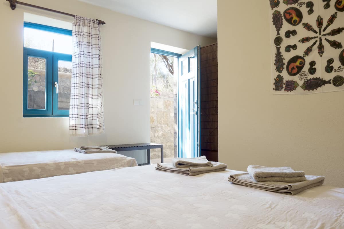 A hotel room with two beds, a window with curtains, a wall with a decorative pattern, and a stack of towels on the bed.