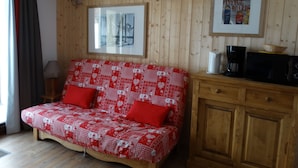 A cozy room with a red and white patterned sofa, a wooden cabinet, a framed picture on the wall, and a window with curtains.