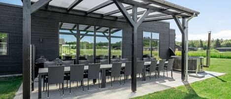 An outdoor patio with a covered seating area, large windows, and a view of the surrounding landscape.