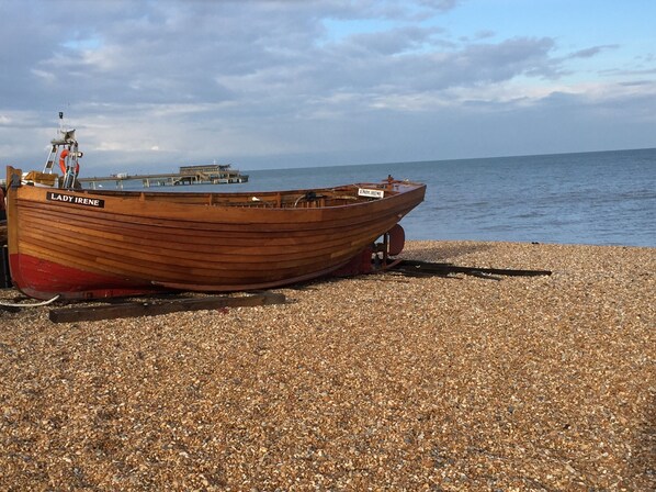 A wooden boat named 'Lady Irene' on a pebbled beach with a pier and calm sea in the background.
