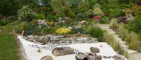 Un jardín con un sendero de grava, rocas y un hogar para fuego.