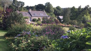 A stone house with a sloped roof and a garden with various plants and flowers.
