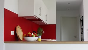 Una cocina con una pared de acento roja, armarios blancos y un cuenco de fruta en la encimera.