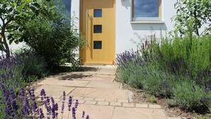 Una casa con una puerta amarilla, un sendero de piedra y plantas de lavanda.