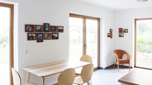 Un comedor con una larga mesa y sillas, una silla de mimbre, y una pared con cuadros enmarcados.