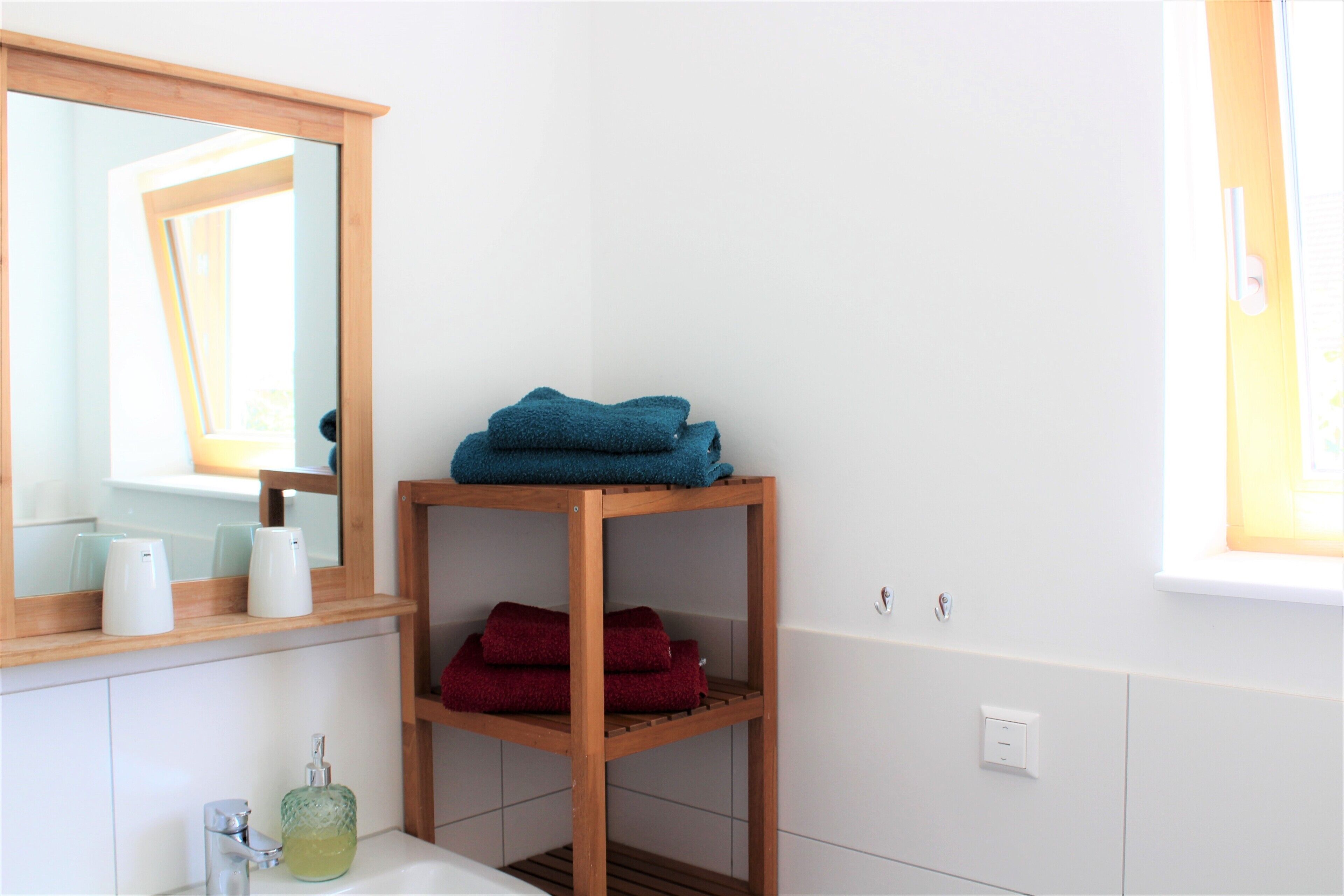 Une salle de bain avec une étagère en bois où sont posés des serviettes, un miroir et un lavabo équipé d’un distributeur de savon.