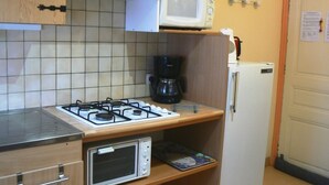 Una cocina compacta con estufa a gas, microondas, cafetera y refrigerador.