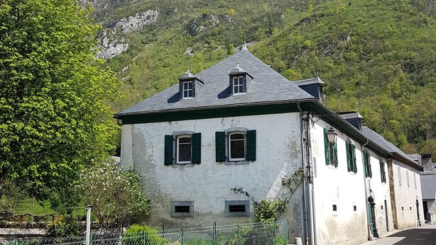 Ein zweistöckiges Gebäude mit geneigtem Dach, grünen Fensterläden und einer Steinverkleidung.