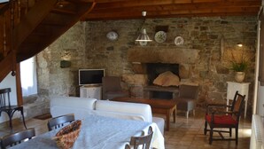 Un interior rústico con chimenea de piedra, vigas de madera, un comedor con mesa y sillas, y un televisor.