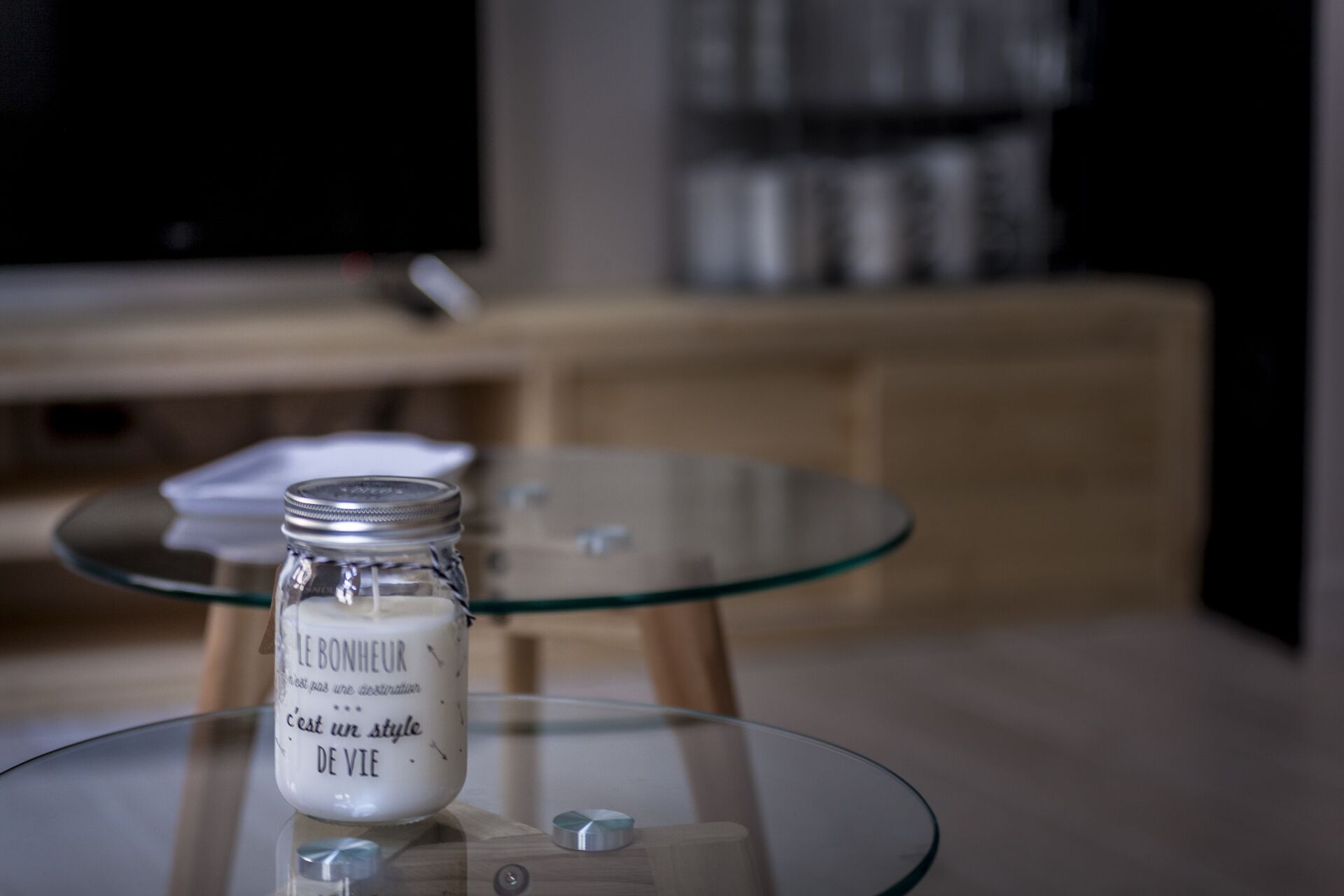 A glass table with a candle labeled 'LE BONHEUR' in a room with a TV and wooden furniture.