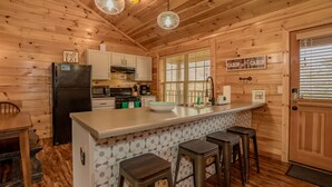 Una cocina de cabaña con paredes de madera, una isla central con taburetes, un refrigerador, una estufa y un lavaplatos.