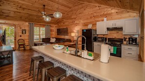 Interior de una cabaña de madera con cocina, comedor y taburetes de bar.