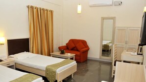 A hotel room with two beds, a red armchair, a small table, a desk, a mirror, and a television.