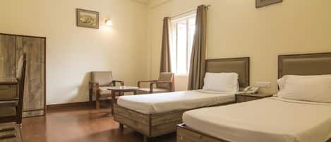 Una camera d'albergo con due letti singoli, una scrivania in legno, una sedia, un tavolino e un armadio.