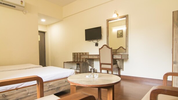 A hotel room with a bed, a desk with a chair, a round table, a television, and a mirror.